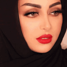 a woman wearing a hijab and red lipstick is looking at the camera .