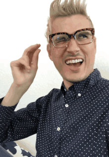 a man wearing glasses and a blue polka dot shirt is smiling