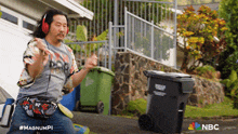 a man wearing headphones and a fanny pack is dancing on the sidewalk in front of a garbage can .