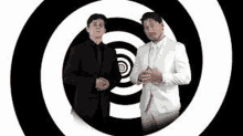 two men in suits are standing next to each other in front of a hypnotic spiral .