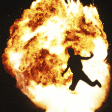 a silhouette of a man jumping in front of a large explosion