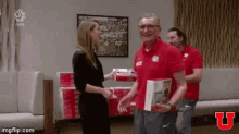 a man in a red shirt is shaking hands with a woman in a black dress in a living room .