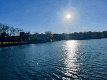 the sun shines brightly over a lake with houses in the background