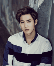 a young man leaning against a wall wearing a blue and white shirt