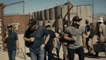 a group of men are walking in the desert and one of them is wearing a hat with the letter t on it