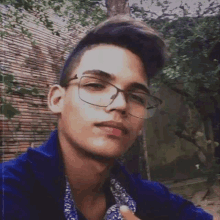 a young man with glasses and a blue shirt is taking a selfie .