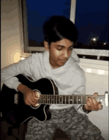 a young man playing a guitar in front of a window