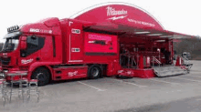 a red milwaukee truck is parked in a parking lot with a trailer attached to it .