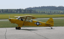 a small yellow u.s. army plane is parked on the runway