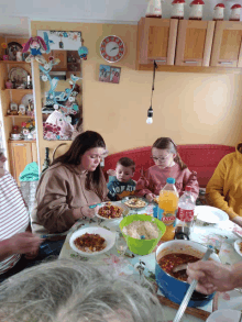 a group of people are sitting at a table with a bottle of orange juice and a bowl of food