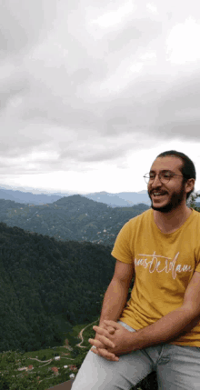 a man wearing a yellow shirt that says amsterdam sits on a hillside