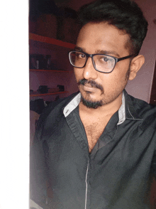 a man wearing glasses and a black shirt is standing in front of a wall