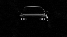 the front of a black car with the headlights lit up in the dark