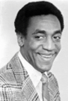 a black and white photo of a smiling man wearing a suit and tie .