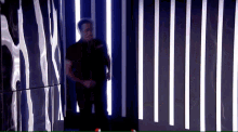 a man in a black shirt is walking through a dark room with a lot of lights on the wall .