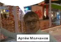 a boy wearing glasses is standing in front of a sign that says " artem molchanov "