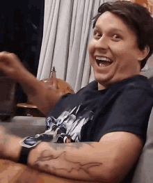 a man with a tattoo on his arm is smiling and wearing a shirt with a shark on it