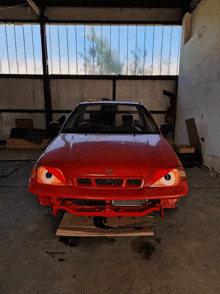 a red suzuki car is parked in a shed