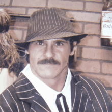 a man with a mustache wearing a hat and striped suit