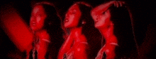 three women are standing next to each other in a dark room with red lights .