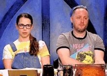 a man and a woman are sitting at a table with a man wearing a shirt that says " never forget "