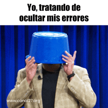 a man covering his face with a blue bucket with the words yo tratando de ocultar mis errores