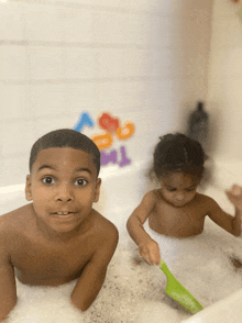 a boy and a girl are playing in a bathtub with foam letters on the wall behind them