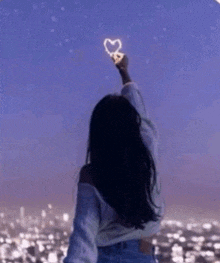 a woman is holding a light in the shape of a heart in the sky .