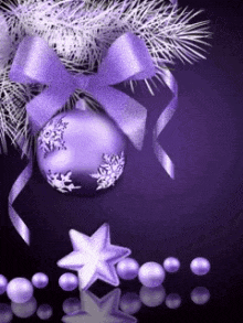 a purple christmas ornament with a bow is hanging from a christmas tree branch