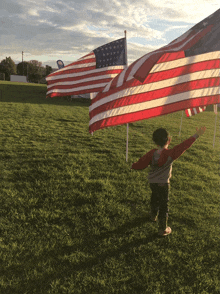 a young boy stands in a field with a large american flag in the background