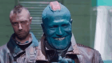 a man with blue paint on his face and a mohawk is smiling .