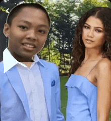 a boy in a suit and a woman in a blue dress are posing for a picture .