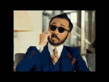 a man with a beard and mustache wearing sunglasses and a suit is talking on a cell phone .