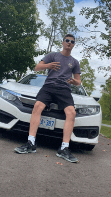 a man kneeling in front of a white honda civic with a license plate that says a 387