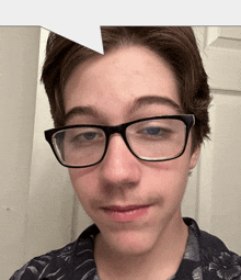 a young man wearing glasses and a floral shirt looks at the camera