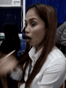 a woman in a white shirt is making a surprised face while sitting at a desk in an office .