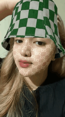 a woman wearing a green and white checkered bucket hat has gucci letters on her face