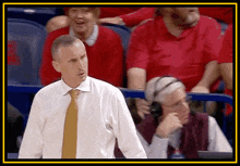 a man in a white shirt and gold tie stands in front of a crowd of people wearing red shirts