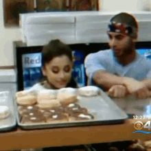 a man and a girl are sitting at a table with a tray of donuts and a sign that says red on it