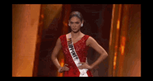 a woman in a red dress with a sash that says philippines on it is standing on a stage .