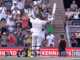 a cricket player holds up his bat in front of a crowd with a sign that says kenna on it