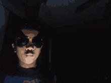 a person wearing sunglasses in the dark with a blue shirt on