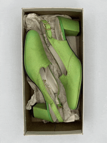 a pair of green shoes in a cardboard box with a buckle on the front