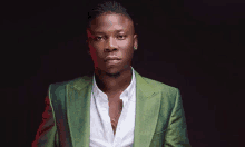 a young man wearing a green suit and a white shirt is standing in front of a black background .