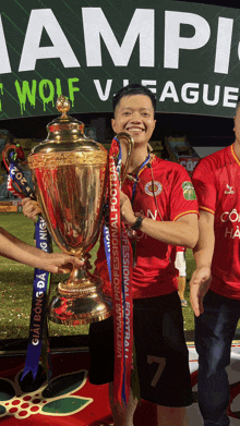 a man in a red shirt is holding a trophy with a ribbon that says vietnam professional football