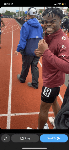 a man in a maroon shirt with the number 8 on his shorts stands on a track