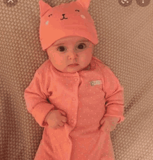 a baby wearing a cat hat and a pink outfit is laying on a bed .