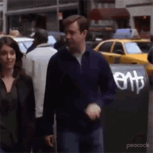 a man and a woman are walking down a street in front of a trash can with the word ent written on it .