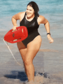 a woman in a black swimsuit is running on the beach holding a life preserver