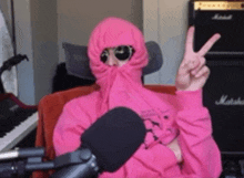 a man wearing a pink hoodie and sunglasses is giving a peace sign